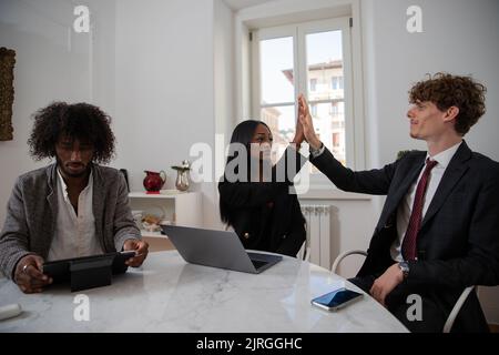 Multi-ethnic working group in the office, African woman and Caucasian man give each other high five, they found an agreement Stock Photo