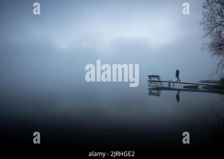 Frau steht auf einem Steg in nebeliger Landschaft, Kochelsee, Deutschland. Stock Photo