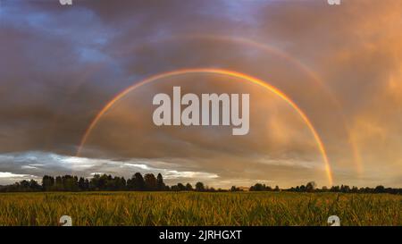 Double rainbow over the field after rain at colorful dramatic sunset Stock Photo
