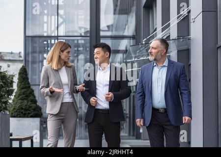 Three diverse business people walking and talking focused and thoughtful seriously outside office building, male and female, discussing plans and work project Stock Photo