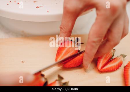 Pastry chef makes delicious red velvet cake. Cutting strawberry and decorating dessert. Stock Photo