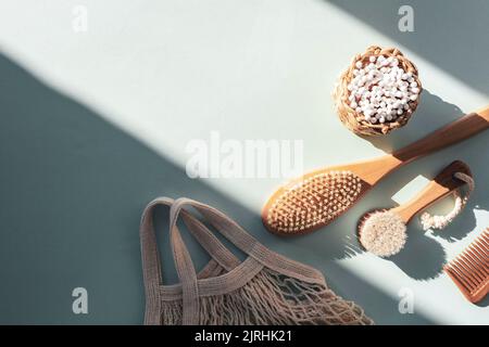 Natural cosmetics, wooden brushes, ear cleaning sticks, comb and mesh bag on light blue table with shadow. Beauty, spa and wellness. Zero waste concep Stock Photo