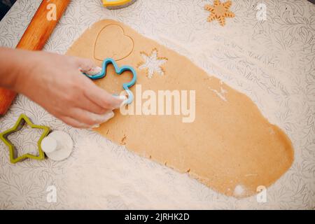 Woman hands form molds cutters ginger dough and makes delicious christmas ginger cookies. Cooking and decorating christmas dessert. Stock Photo