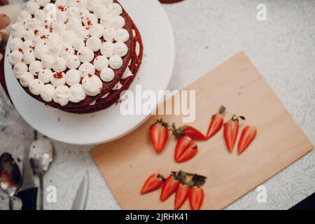 Making delicious red velvet cake. Cooking and decorating dessert with cream cheese and strawberry. Stock Photo