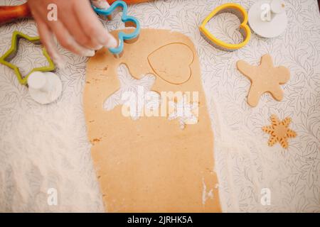 Woman hands form molds cutters ginger dough and makes delicious christmas ginger cookies. Cooking and decorating christmas dessert. Stock Photo