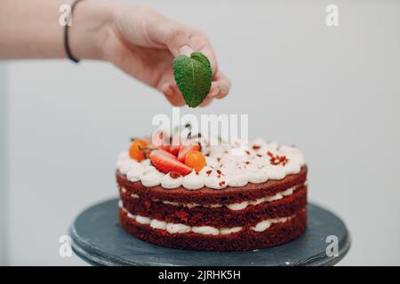 Pastry chef makes delicious red velvet cake. Cooking and decorating dessert. Putting mint leaf Stock Photo