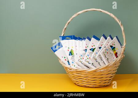Basket with several boxes with twelve colored pencils on yellow green background with copy space Stock Photo