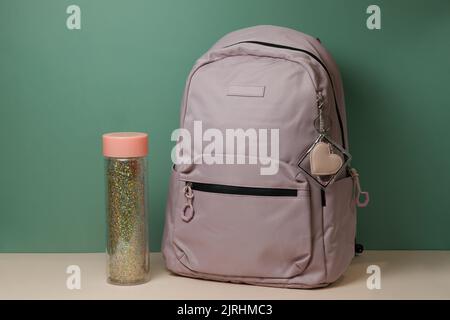 A school backpack with a bottle of water on a table on a green background. Preparation for school Stock Photo