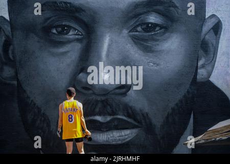 Los Angeles, California, USA. 24th Aug, 2022. Brian Tang wearing Los Angeles Lakers Kobe Bryant's jersey number 8 stands in front of a mural depicting Kobe Bryant and his daughter, Gianna in Los Angeles, Wednesday, August 24, 2022. To mark Mamba Day 2022, a 125 feet by 32 feet giant outdoor mural depicting a close-up of Kobe Bryant's face, in black-and-white, in the middle, flanked by a mamba snake on the left and, in color, a group of children including Bryant's daughter Gianna playing basketball atop a giant book, is unveiled on an entire side of a building near former Staples Center. (Cred Stock Photo