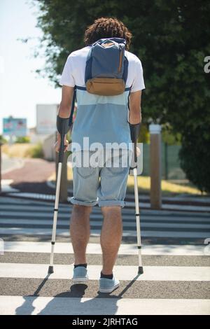 disabled man using crutches to cross the road Stock Photo
