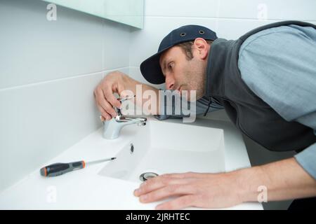 male plumber hand fixing tap of sink in bathroom Stock Photo