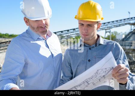 group of engineers wearing hardhats discussing over plans Stock Photo