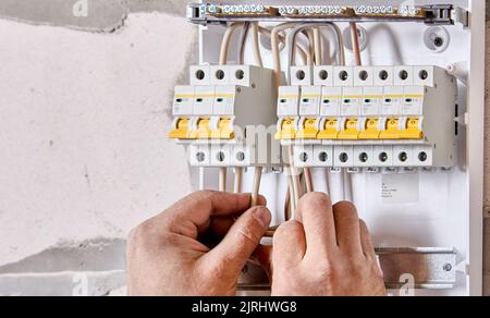 An electrician connects wires to fuse box in consumer unit of electrical panel. Stock Photo