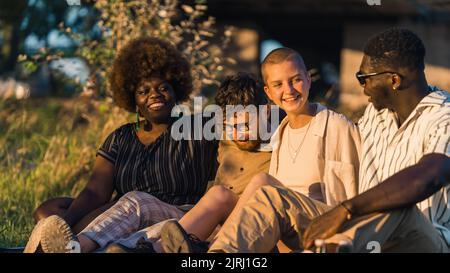 Group of happy young people having a weekend picnic in nature, sitting together on the grass near the campfire, talking and laughing. Sunset time. High quality photo Stock Photo