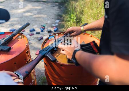 Unrecognizable European man touching, cleaning, and changing clip of a rifle placed on metal orange barrels. Outdoor shot. High quality photo Stock Photo