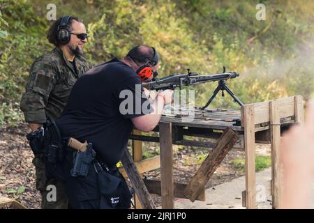 08.07.2022 Warsaw, Poland Machine gun competition. Medium long outdoor shot of two caucasian man in military-like clothes and protective gun range gear using machine gun. High quality photo Stock Photo