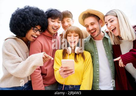 Group of young cheerful people watching something funny on mobile phone. Excited students using their cell technological devices. Concept of young Stock Photo