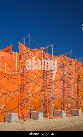 A commercial building is covered with orange plastic sheeting during renovation work to contain dust and debris. Stock Photo