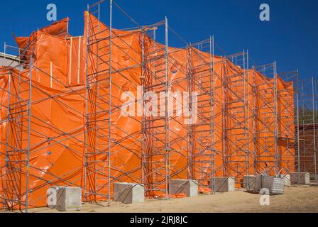 A commercial building is covered with orange plastic sheeting during renovation work to contain dust and debris. Stock Photo