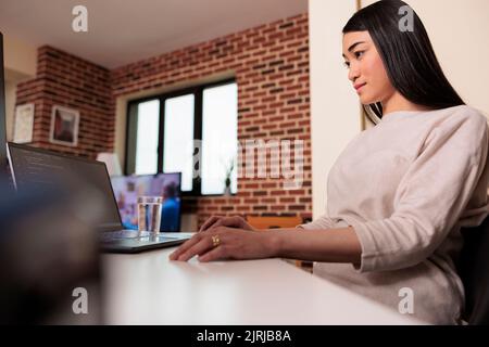 Asian programmer coding software app with html script, using firewall server encryption for web app development. Female coder programming new user interface on multiple monitors. Stock Photo