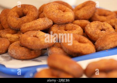 A number of plain fresh golden fried cinnamon sugar doughnuts or donuts stacked on a blue tray and baking paper Stock Photo