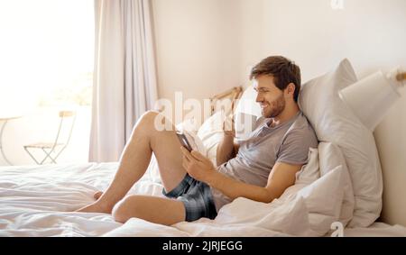 Relax man in bed, using phone and happy while drinking coffee in the morning reading emails, using internet or social media. Person using smartphone Stock Photo