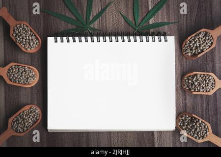 cannabis seeds and hemp leaf on a blank notebook, space for text. Stock Photo