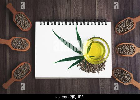 Hemp oil and hemp leaf on a blank notebook, space for text. Stock Photo
