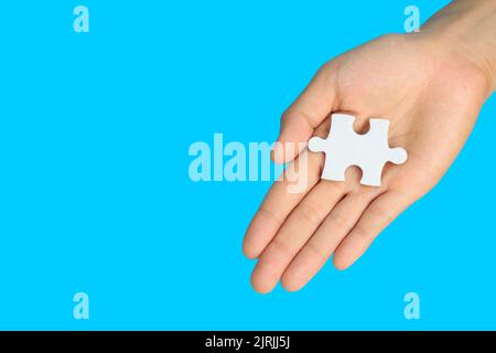 white jigsaw puzzle pieces in  hand on blue background, The last piece of jigsaw puzzle, Copy space. Stock Photo