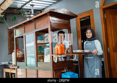 smiling two sellers in apron preparing chicken noodles dish Stock Photo