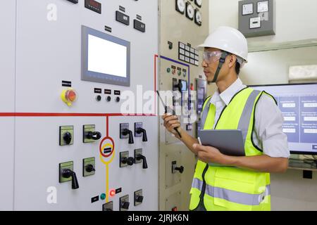 Experienced electrician working in power plant control room. Engineer working on the checking status switchgear electrical energy distribution substat Stock Photo