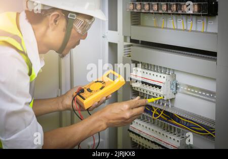 Electrical engineers test the voltage and current of the wires in the electrical cabinet control.the multimeter is in the hands of the electrician det Stock Photo