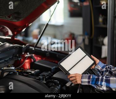 Caucasian female auto mechanic changes the engine air filter in the car. Stock Photo