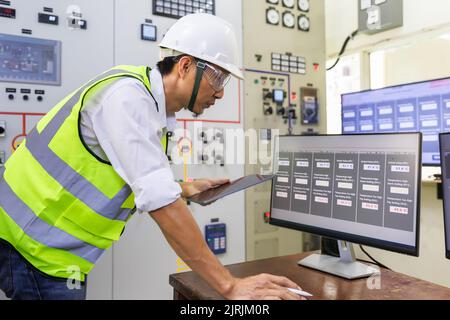 Experienced electrician working in a power plant control room. Engineer working in electric power distribution substation checking status. Machine ope Stock Photo