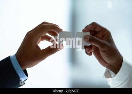 Its the perfect fit. Closeup shot of two unidentifiable businesspeople holding puzzle pieces together. Stock Photo