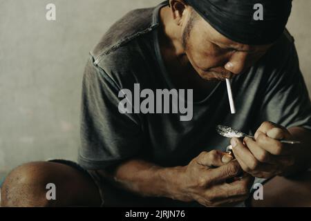 Drug addicts in the dark room. Addict/junkie preparing drugs with a spoon and lighter. White powder and a syringe. Drug concept. International drug ab Stock Photo