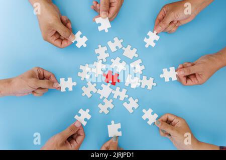 Hands of diverse people assembling jigsaw puzzle, team put pieces together searching for right match, help support in teamwork to find common solution Stock Photo