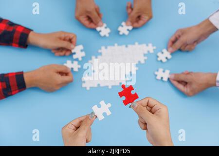 Hands of diverse people assembling jigsaw puzzle, team put pieces together searching for right match, help support in teamwork to find common solution Stock Photo