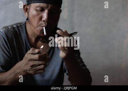 Drug addicts in the dark room. Addict/junkie preparing drugs with a spoon and lighter. White powder and a syringe. Drug concept. International drug ab Stock Photo