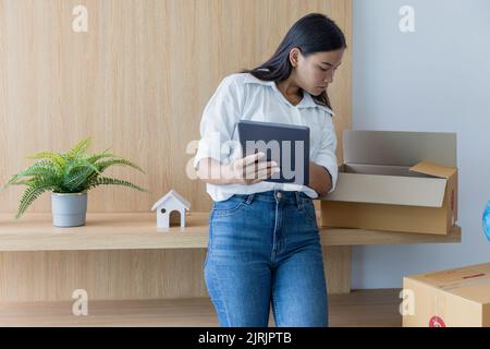 woman holding a tablet checking a cardboard box Packing stuff to move to a new house. Stock Photo