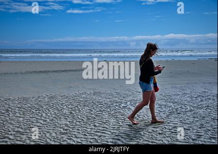 Mature woman walking on the beautiful beach and using mobile phone Stock Photo