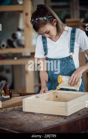 happy attractive hardworking middle aged professional female carpenter worker looking and choosing wood in the workshop. Stock Photo