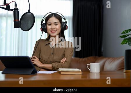 Professional and talented young Asian female blogger podcaster in her home studio, using recording equipment to running her online radio show. Stock Photo