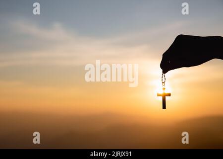 Human hand holding Christian cross with a sunset sky background Stock ...