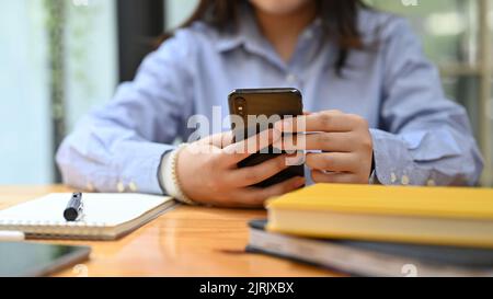cropped and close-up hands image, A businesswoman or female office worker using her smartphone at her office desk, texting with her friends, scrolling Stock Photo