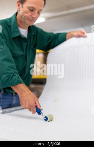 Tauberbischofsheim, Germany. 18th Aug, 2022. An employee of the manufacturer of infrared heaters Vitramo fixes the heating mat in an infrared heater for wall mounting in the company's production. In an infrared heater, a frontal cover (glass or sheet metal) is heated from the back by a heating layer that converts electrical energy into heat. Credit: Daniel Karmann/dpa/Alamy Live News Stock Photo