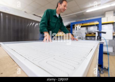 Tauberbischofsheim, Germany. 18th Aug, 2022. An employee of the manufacturer of infrared heaters Vitramo fixes the heating mat in an infrared heater for wall mounting in the company's production. In an infrared heater, a frontal cover (glass or sheet metal) is heated from the back by a heating layer that converts electrical energy into heat. Credit: Daniel Karmann/dpa/Alamy Live News Stock Photo