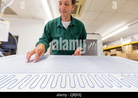 Tauberbischofsheim, Germany. 18th Aug, 2022. An employee of the manufacturer of infrared heaters Vitramo fixes the heating mat in an infrared heater for wall mounting in the company's production. In infrared heating, a frontal cover (glass or sheet metal) is heated from the back by a heating layer that converts electrical energy into heat. Credit: Daniel Karmann/dpa/Alamy Live News Stock Photo