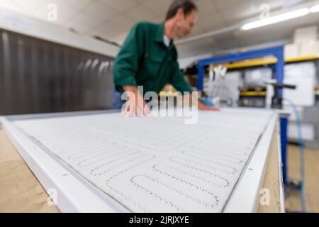 Tauberbischofsheim, Germany. 18th Aug, 2022. An employee of the manufacturer of infrared heaters Vitramo fixes the heating mat in an infrared heater for wall mounting in the company's production. In an infrared heater, a frontal cover (glass or sheet metal) is heated from the back by a heating layer that converts electrical energy into heat. Credit: Daniel Karmann/dpa/Alamy Live News Stock Photo