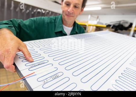 Tauberbischofsheim, Germany. 18th Aug, 2022. An employee of the manufacturer of infrared heaters Vitramo fixes the heating mat in an infrared heater for wall mounting in the company's production. In an infrared heater, a frontal cover (glass or sheet metal) is heated from the back by a heating layer that converts electrical energy into heat. Credit: Daniel Karmann/dpa/Alamy Live News Stock Photo